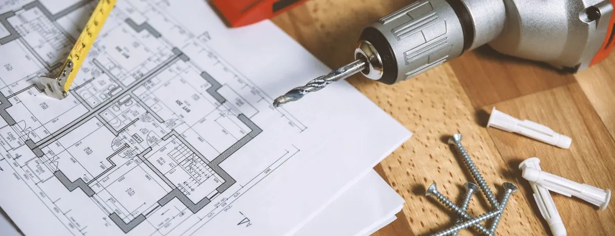 A floor plan on a workbench beside a spirit level, a drill and screws