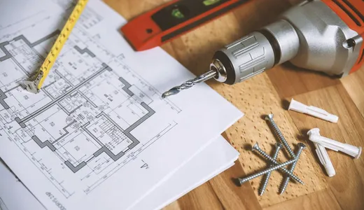 A floor plan on a workbench beside a spirit level, a drill and screws