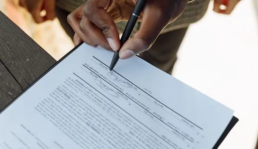 A person signing a printed document held on a clipboard