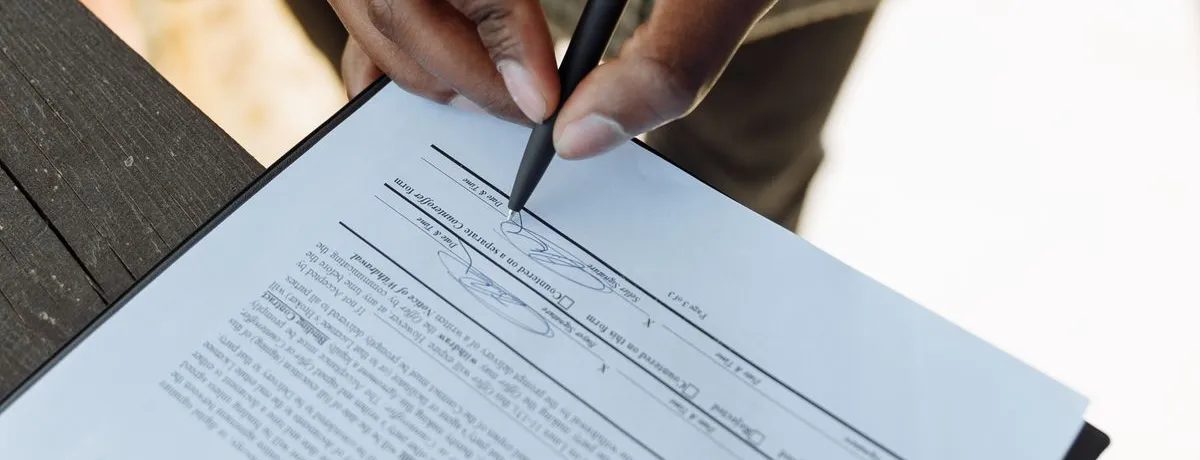 A person signing a printed document held on a clipboard